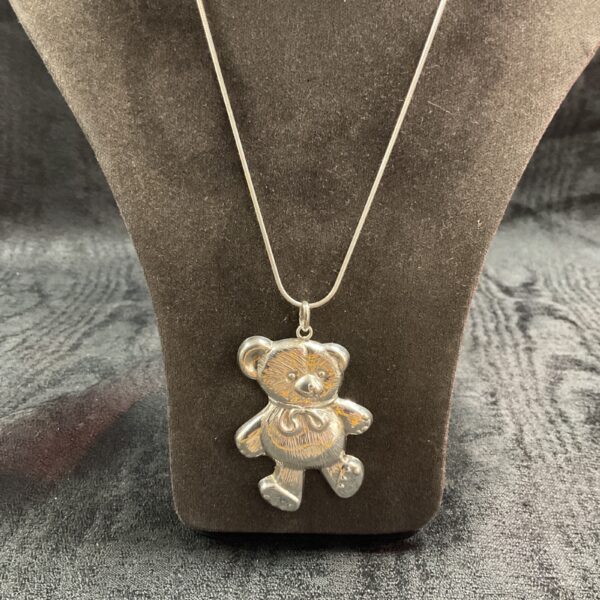 Close-up of silver teddy bear pendant on necklace.