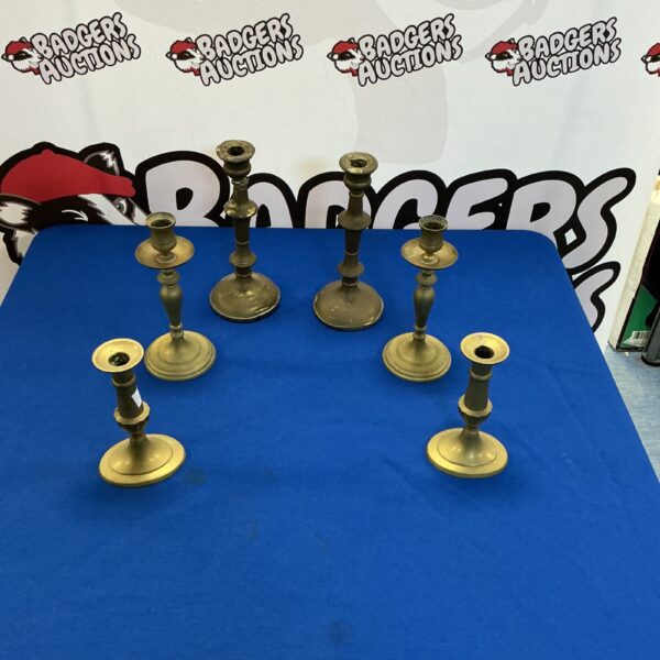 Six antique brass candle sticks on a dark background.