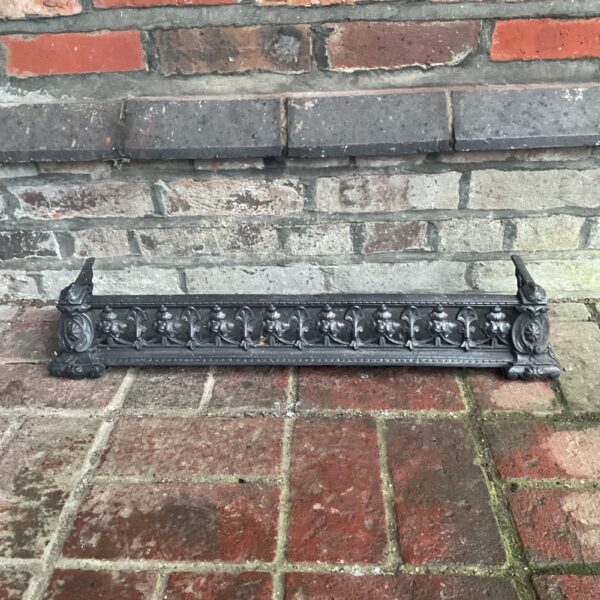 Intricate Victorian cast iron fireplace fender with floral details.