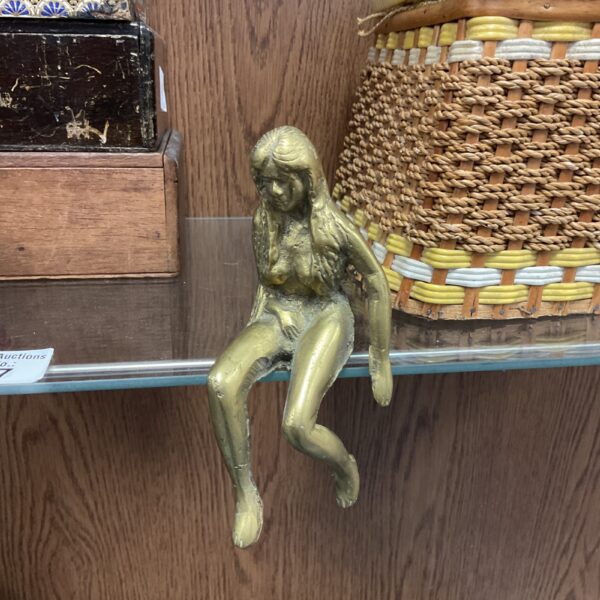 Vintage brass nude sculpture on wooden shelf.