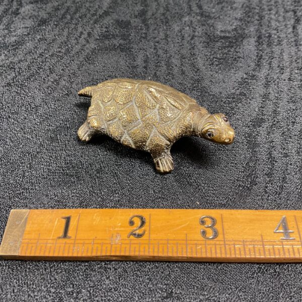 Vintage brass turtle paperweight with glass eyes on a dark surface.
