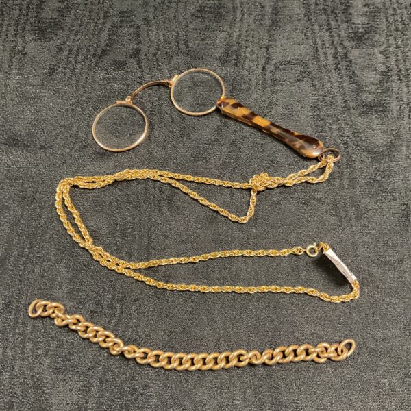 Vintage lorgnette glasses and rolled gold necklace on dark background.