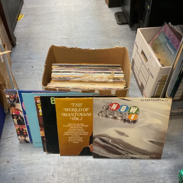 Mixed vinyl record collection in a cardboard box.