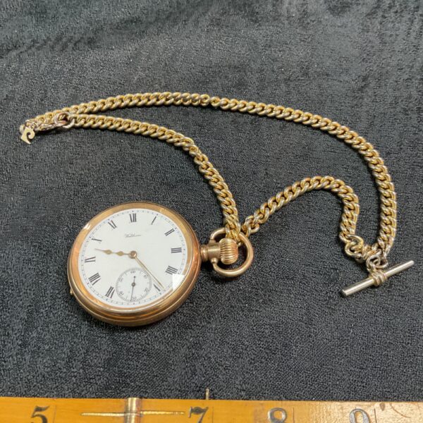 Vintage Waltham pocket watch with gold chain displayed on a surface.