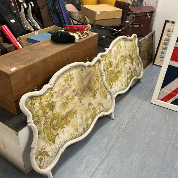 Antique French padded headboard with floral fabric and curved frame.