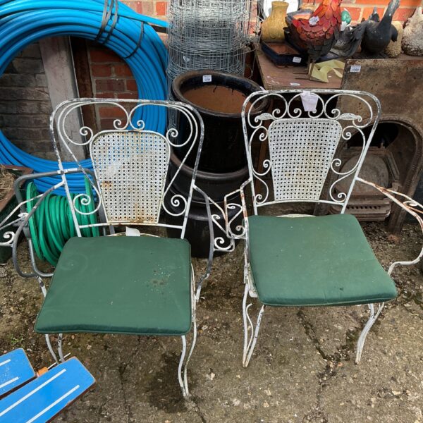 Pair of antique metal garden chairs in a garden setting.