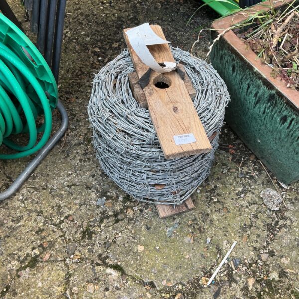 Used roll of galvanised barbed wire on a wooden spool.