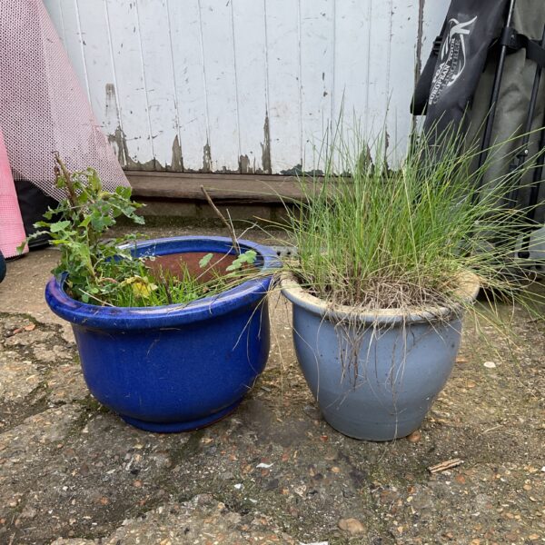 Two blue glazed ceramic garden pots in a garden setting.