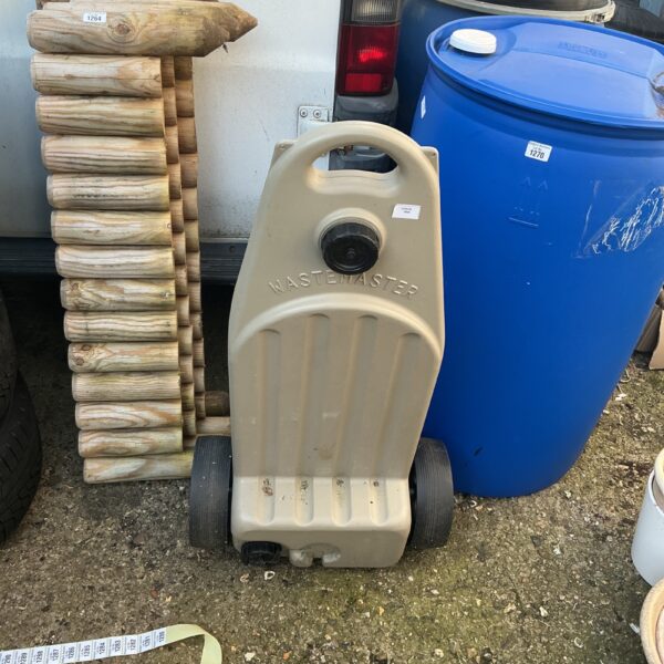 Grey camping waste tank with wheels, a ‘Waste Master’ for outdoor use.