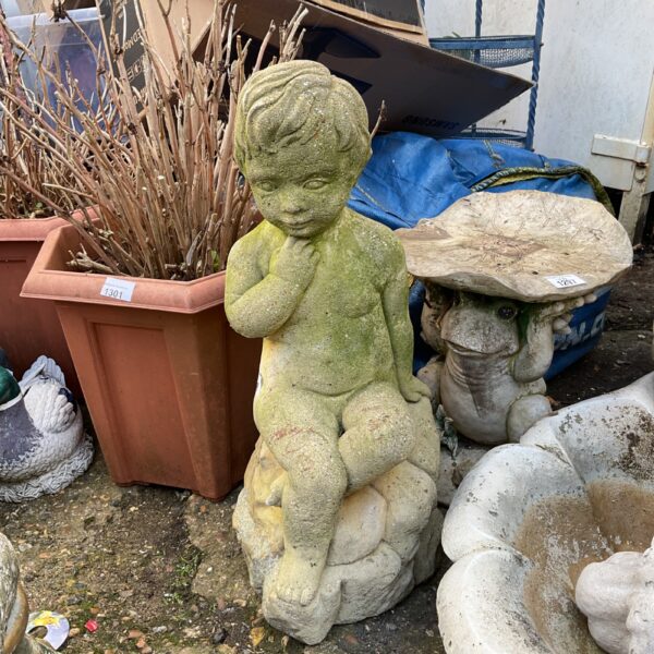 Large weathered cherub garden ornament in a garden setting.
