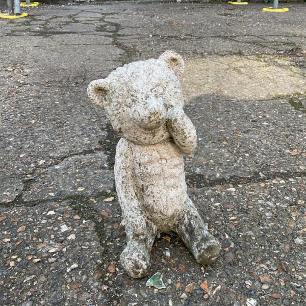 Vintage concrete garden teddy bear ornament in a garden setting.