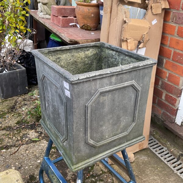 Modern fibreglass cube planter with metal stand in a garden setting.
