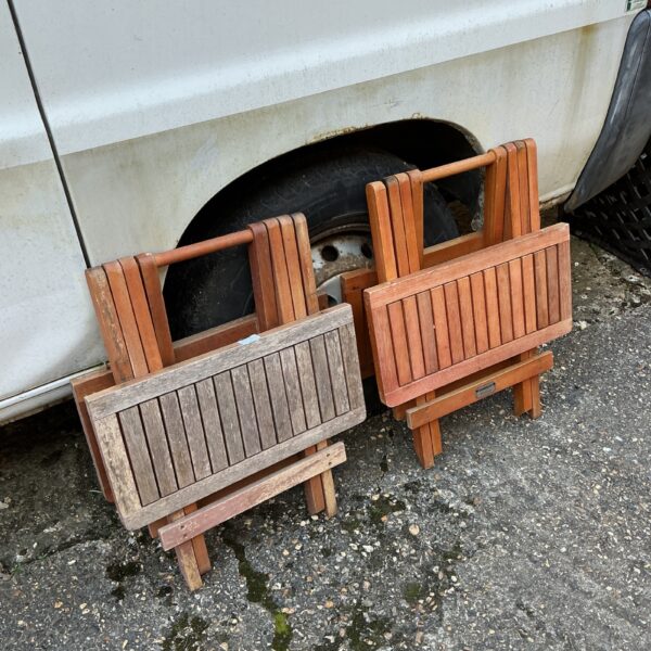 Two weathered wooden folding garden tables in a garden setting.