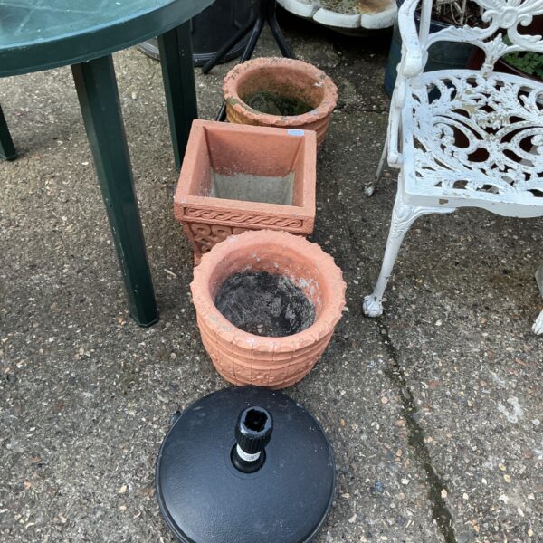 Three terracotta garden pots and a parasol base in a garden setting.