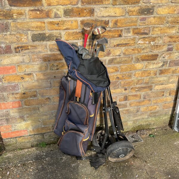 Blue golf bag with trolley and golf clubs on pavement.
