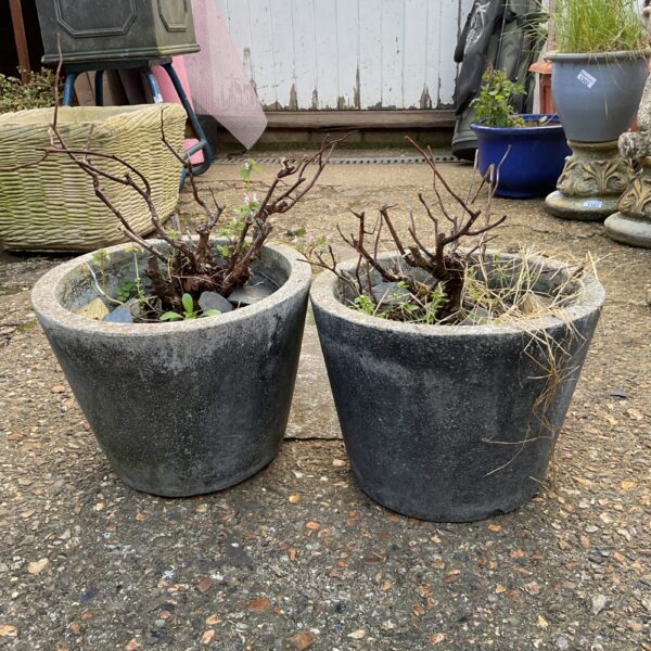 Two weathered granite plant pots in a garden setting.