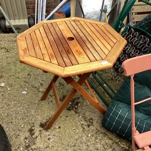 Rustic hexagonal wooden garden table with folding legs in a garden setting.