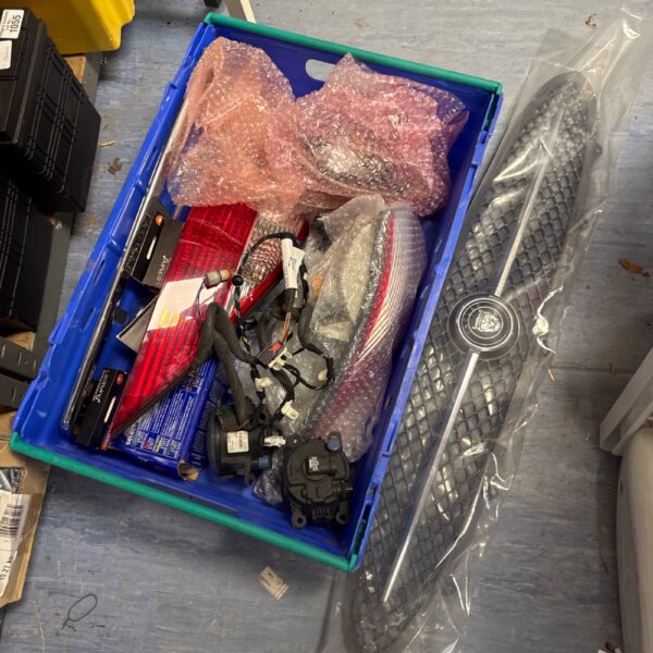 Assorted Jaguar parts including a grille and lights in a blue crate.