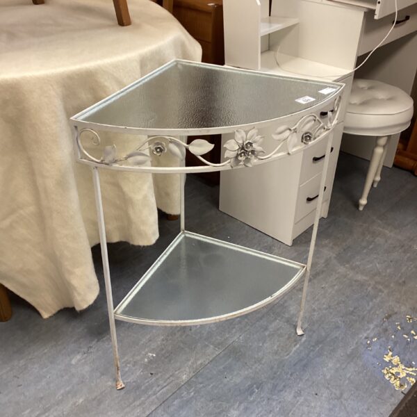 Vintage metal corner table with glass top and floral details.