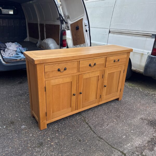 Solid oak sideboard cabinet with three doors and a drawer.