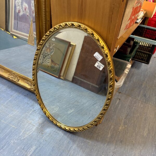 Antique oval gilt mirror with bevelled glass and decorative frame.
