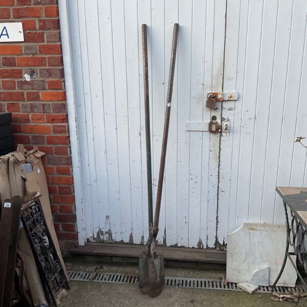 Pair of vintage post hole digging spoons leaning against a wall.