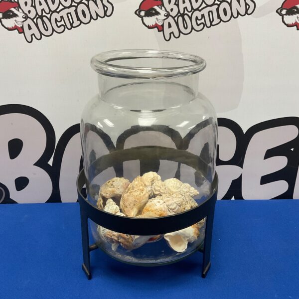 Clear glass jar displaying a collection of seashells on a stand.