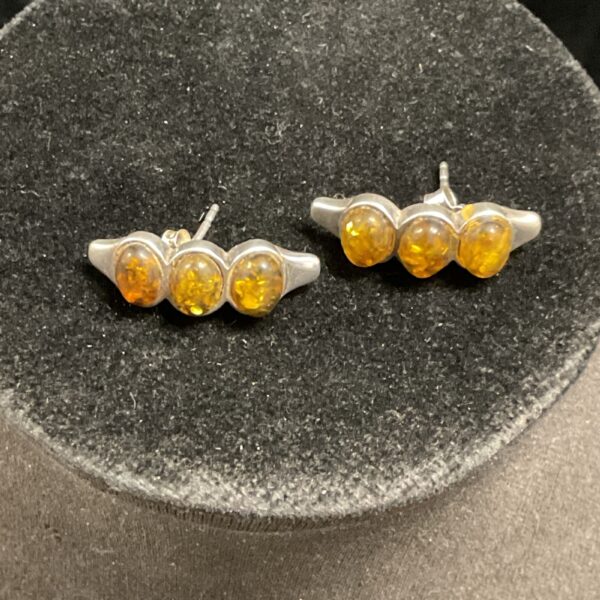 Close-up of silver amber stud earrings with warm honey tones.