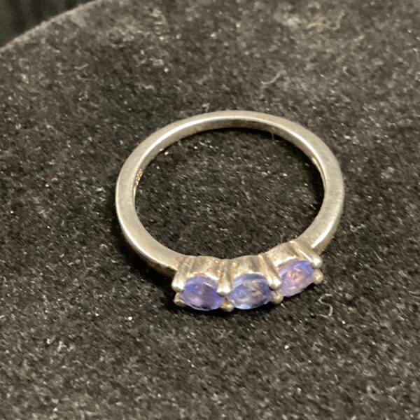 Close-up of a silver ring with three amethyst gemstones.