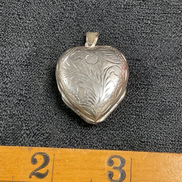 Close-up of silver clover heart locket with floral engraving.