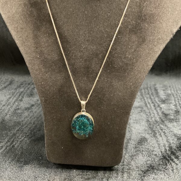 Close-up of silver necklace with green resin pendant.