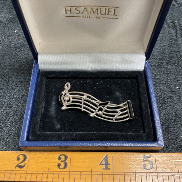 Vintage silver musical brooch with treble clef and staff.