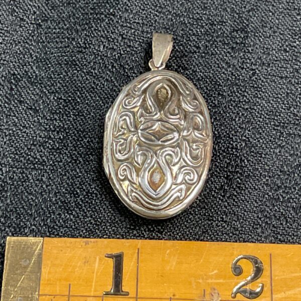 Vintage silver locket with intricate scrollwork design.