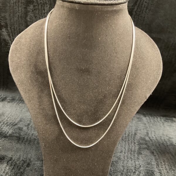 Layered silver snake chain necklaces on display.