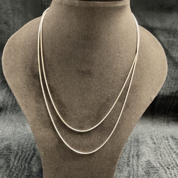 Pair of delicate silver snake chain necklaces on display.