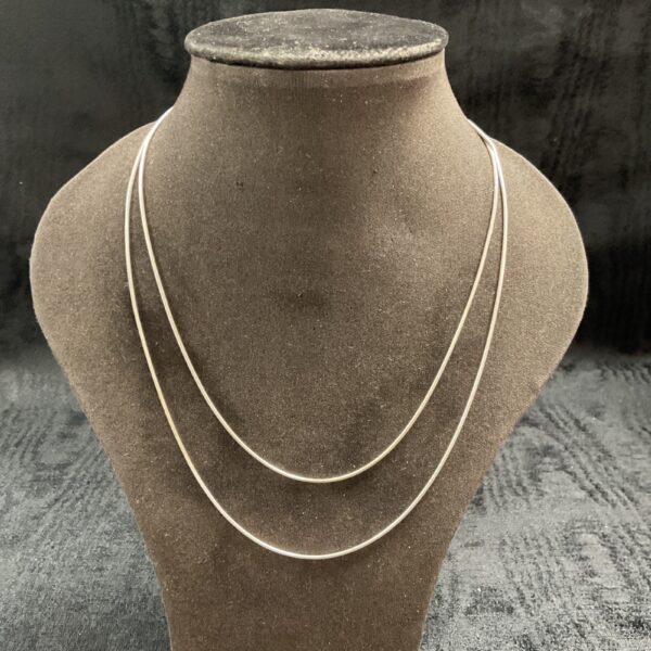 Pair of delicate silver snake chain necklaces on display.