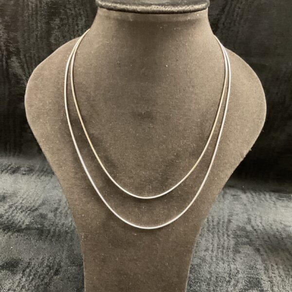 Two sterling silver snake chain necklaces on a display bust.