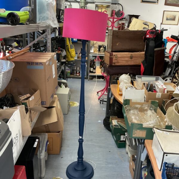 Vintage blue standard lamp with pink shade in a cluttered room.