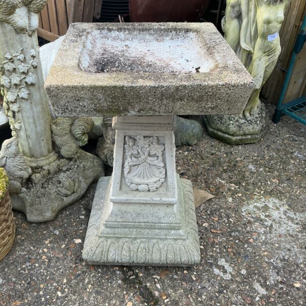 Classic stone effect bird bath in a garden setting.