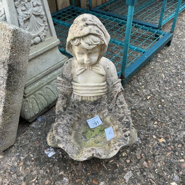 Vintage stone effect bird bath with a young girl statue in a garden.