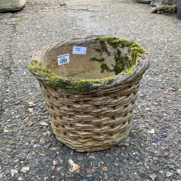 Close-up of a stone wicker basket planter in a garden setting.