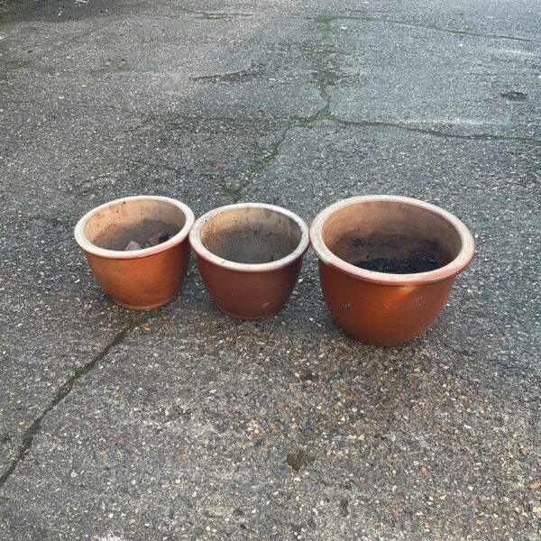 Three terracotta plant pots in a garden setting.