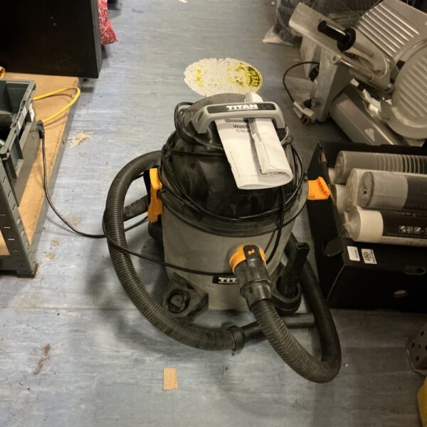 Titan wet/dry vacuum cleaner with hose attached, workshop cleaning.