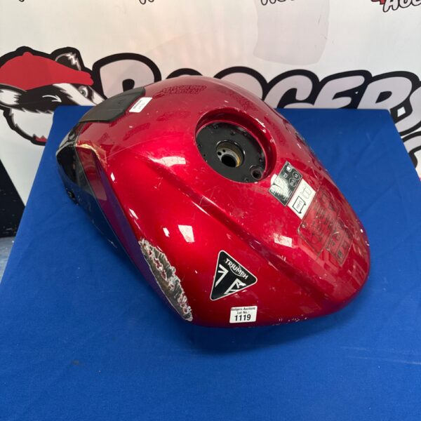 Red Triumph fuel tank for motorcycle restoration with dents.
