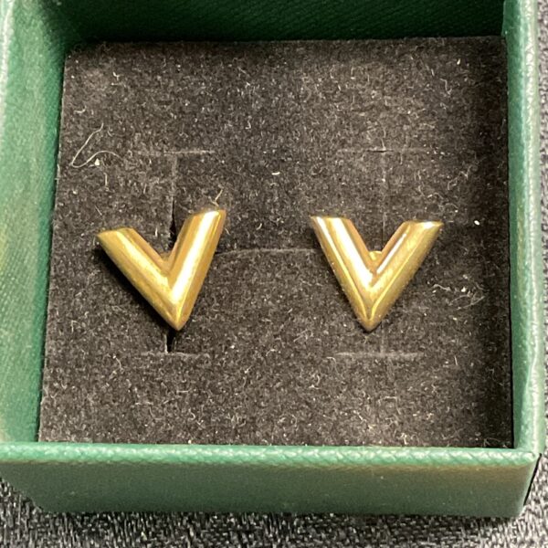 Gold plated V Versace style stud earrings on a dark background.