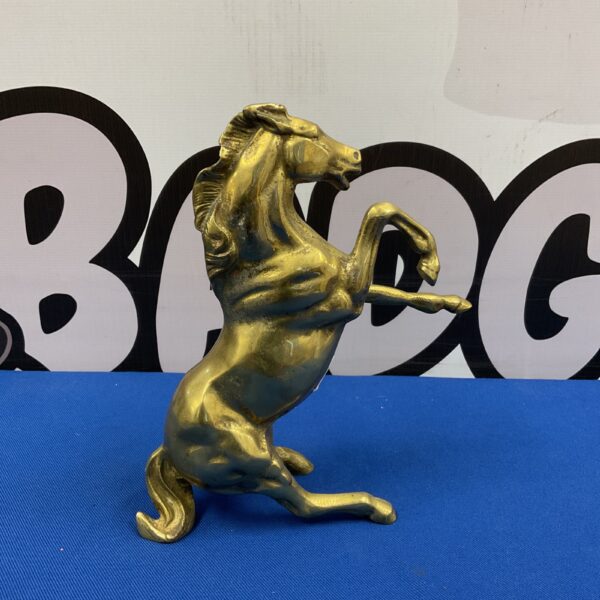 Vintage brass rearing horse sculpture on blue surface.