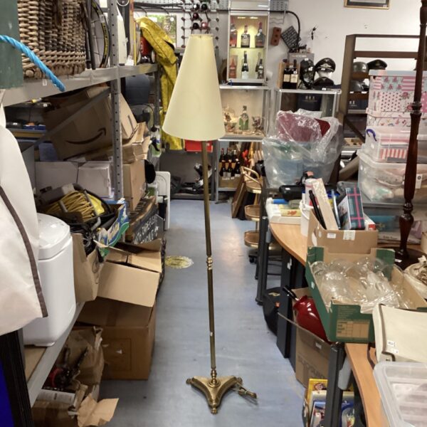 Vintage brass standard lamp with claw feet in a cluttered room.