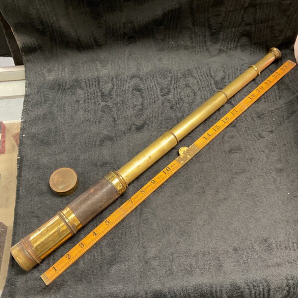 Full view of a vintage brass four-draw telescope on a chair.