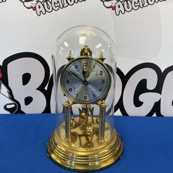 Front view of a vintage German brass torsion clock under a glass dome.