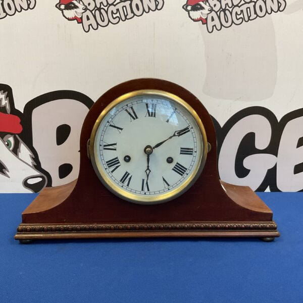 Front view of a vintage wooden mantle clock with brass dial.